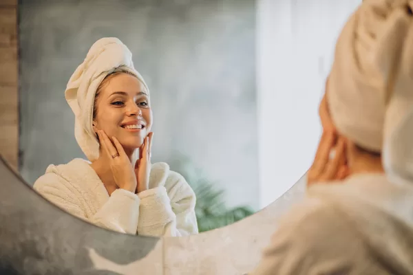 Mulher sorridente cuidando da pele em frente ao espelho, após aplicar máscara facial natural em casa.