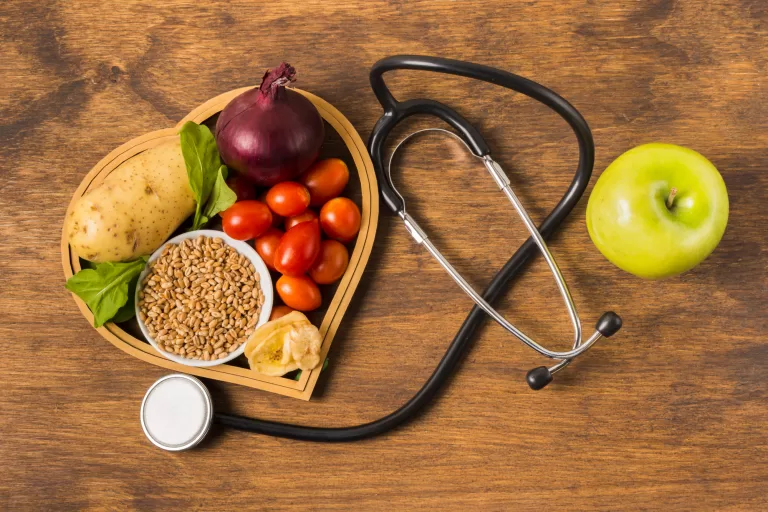 Alimentação natural para saúde do coração com vegetais, grãos e maçã verde ao lado de estetoscópio.