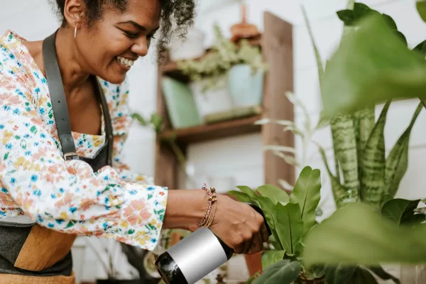 Mulher sorridente regando plantas verdes em horta caseira dentro de casa.