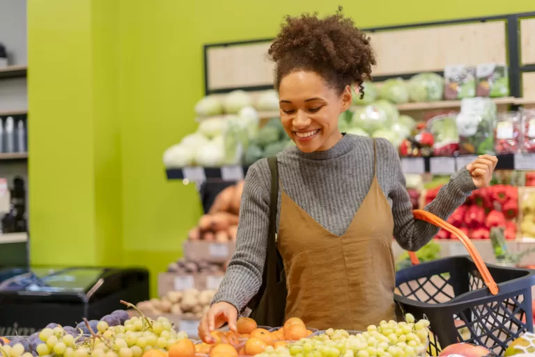 Mulher escolhendo frutas frescas no mercado, fazendo compras saudáveis com foco em alimentação natural e consciente.